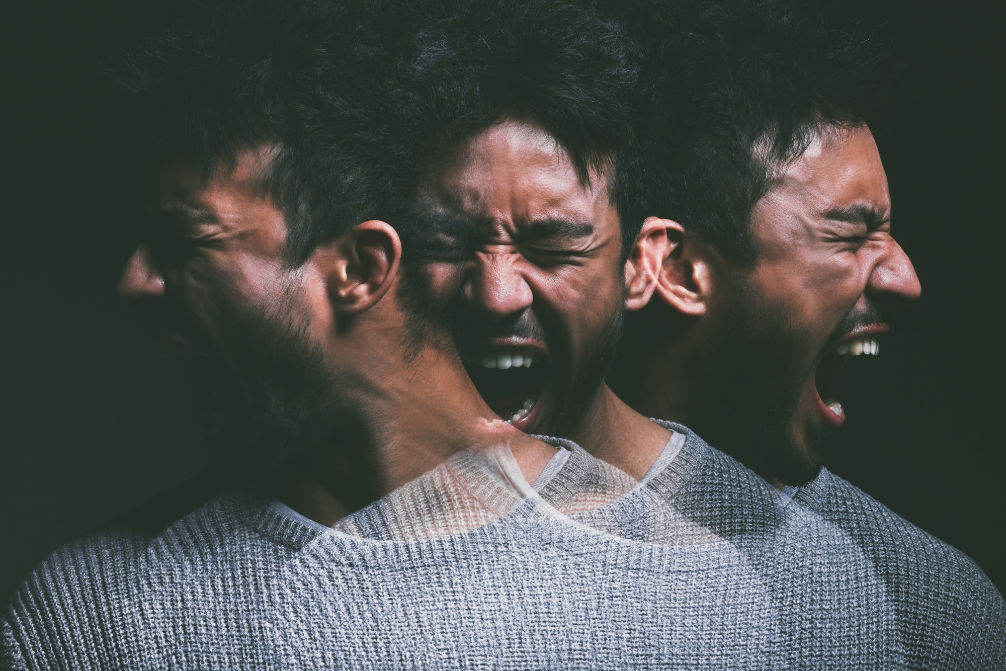 Studio shot of a young man experiencing mental anguish and screaming against a black background