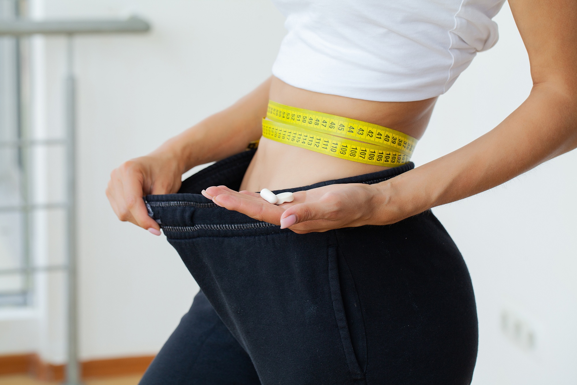 Woman measuring her waist with many slim pills in her hand