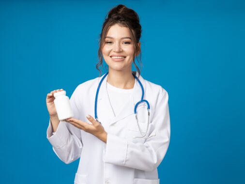 Young woman with stethoscope and jar of pills in hands on blue background
