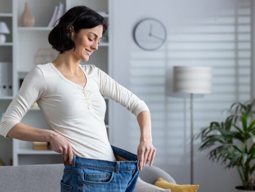 Happy woman showing weight loss by wearing old jeans at home